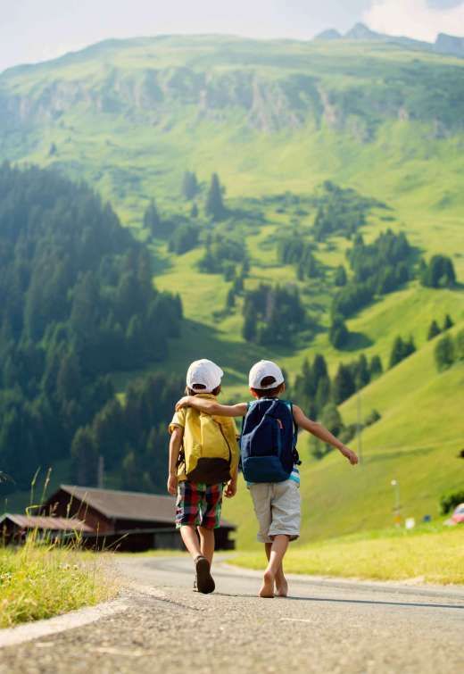 Two little children, boy brothers with backpacks travel on the road to scenic mountains, summertime